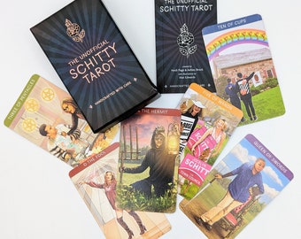 May include: A set of tarot cards featuring characters and scenes from the television show Schitt's Creek. The cards are in a black box with gold lettering that reads "The Unofficial Schitty Tarot".