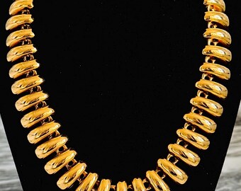 May include: A gold-toned necklace with a chunky, rounded chain design. The necklace is made of multiple linked, round, hollow pieces.