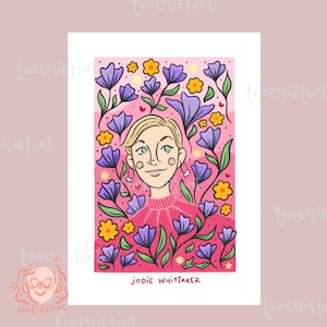 Peut inclure: Une illustration numérique d'une femme aux cheveux blonds courts, portant un pull rose, entourée de fleurs violettes et jaunes sur un fond rose. Le texte "JODIE WHITTAKER" est en bas de l'image.