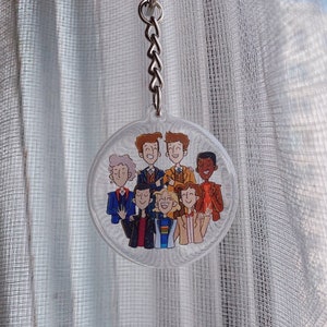 Peut inclure: Un porte-clés rond et transparent avec une illustration colorée de huit personnages de dessin animé. Les personnages sourient tous et semblent être amis. Le porte-clés est un excellent moyen de montrer votre fandom pour une émission de télévision populaire.
