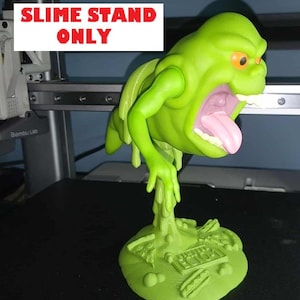 May include: A green Slime stand figure with an open mouth and pink tongue. The stand is green and has the text "Ecto 1" on it. The text "SLIME STAND ONLY" is in a white rectangle above the figure.