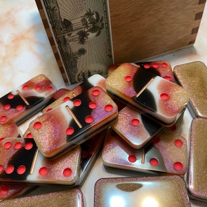 Puede incluir: Un juego de dominó con un acabado brillante multicolor. Los dominós tienen puntos negros y contornos rojos. Los dominós están apilados unos sobre otros.