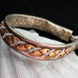 Può includere: Un braccialetto in pelle intrecciata con filo dorato e argentato intrecciato nel design.