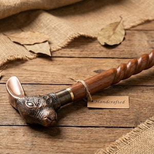 Puede incluir: Bast&oacute;n artesanal con un mango de cabeza de conejo de bronce y un eje de madera retorcida. El bast&oacute;n es marr&oacute;n y tiene una etiqueta que dice "Handcrafted".