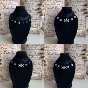 May include: Four black choker necklaces with silver charms on black velvet display stands. Each necklace has a different set of charms, including moon phases, a pentacle, and various colored beads.