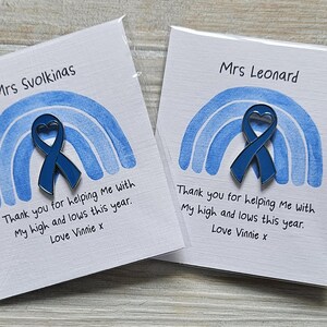 May include: Two square white cards featuring a blue watercolor rainbow graphic and a dark blue awareness ribbon pin with a heart-shaped cutout. The text reads Mrs Svolkinas or Mrs Leonard, Thank you for helping Me with My high and lows this year. Love Vinnie x.