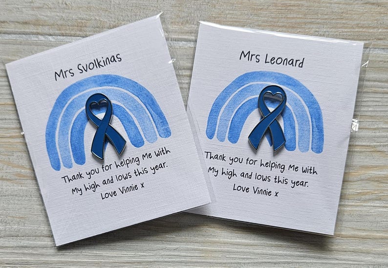 May include: Two square white cards featuring a blue watercolor rainbow graphic and a dark blue awareness ribbon pin with a heart-shaped cutout. The text reads Mrs Svolkinas or Mrs Leonard, Thank you for helping Me with My high and lows this year. Love Vinnie x.