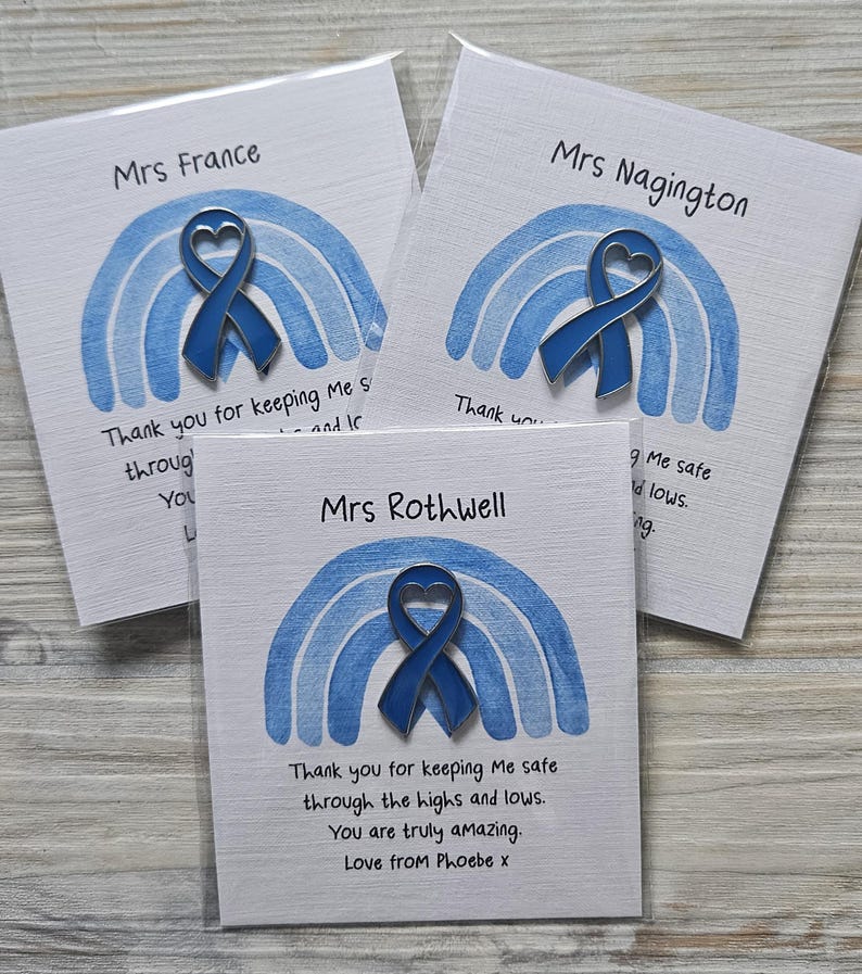 May include: Three blue enamel heart-shaped awareness ribbon pins attached to white cards. Each card features a watercolor-style blue rainbow illustration and printed text including names like Mrs France, Mrs Nagington, and Mrs Rothwell.