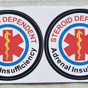 Pu&ograve; includere: Quattro adesivi rotondi con la scritta "Steroid Dependent Adrenal Insufficiency". Presentano una stella rossa con un simbolo medico giallo, circondata da bordi blu e neri, su sfondo bianco.