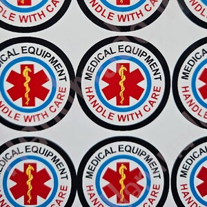 May include: Round black and white stickers with the text "MEDICAL EQUIPMENT HANDLE WITH CARE" in a white circle with a red star of life and a snake wrapped around a staff in the centre.