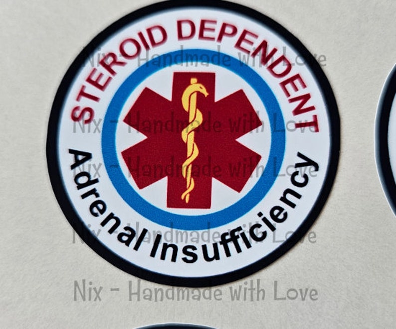 Pu&ograve; includere: Un adesivo rotondo con la scritta "Steroid Dependent Adrenal Insufficiency". Presenta una stella rossa con un simbolo medico giallo al centro, su sfondo bianco, con un bordo nero.