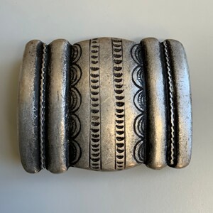 May include: A silver belt buckle with a decorative design of repeating circles and half-circles.