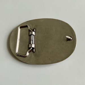 May include: Silver oval belt buckle with a smooth, polished finish. The buckle has a simple, classic design with a single loop for attaching a belt.