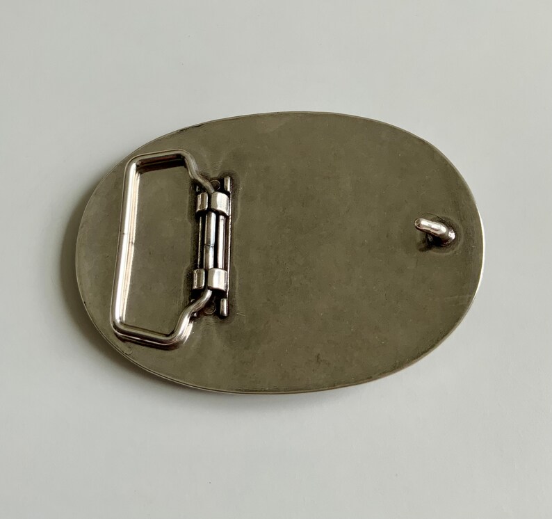 May include: Silver oval belt buckle with a smooth, polished finish. The buckle has a simple, classic design with a single loop for attaching a belt.