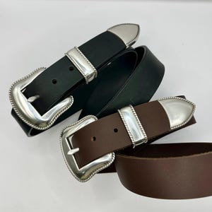 May include: Three leather belts with silver buckles. One is black, the others brown. The buckles have a decorative rope trim. The belts are displayed against a white background.