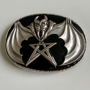 May include: Silver belt buckle with a black enamel background. The buckle features a silver bat with wings spread wide and a pentagram in the center.