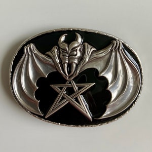 May include: Silver belt buckle with a black enamel background. The buckle features a bat with wings spread wide and a pentagram in the center.