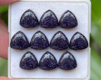 May include: A collection of ten triangular, dark blue gemstones with sparkling inclusions, arranged in a white tray. The polished stones have a smooth, glossy surface, and are held by a hand. The gemstones are a deep, rich blue color.