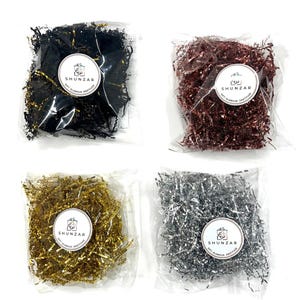 May include: Four bags of shredded paper, each in a different color: black, rose gold, gold, and silver. The bags are labeled with the brand name "Shunzar" and the text "Gift Glamour Gratitude".