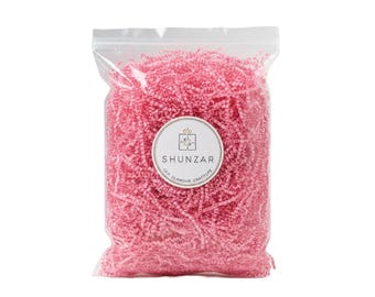 May include: A clear plastic bag filled with pink shredded paper. A white circular label with the text "SHUNZAR" and the phrase "OUT OF GLAMOUR GRATITUDE" is affixed to the front of the bag. The shredded paper is a vibrant pink color.