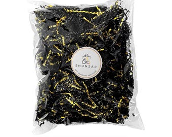 May include: A clear plastic bag filled with black and gold shredded paper. The paper is a mix of black strips with gold metallic accents. A white circular label with the text "SHUNZAR" and the words "GIFT, GLAMOUR, GRATITUDE" is affixed to the bag.
