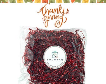 May include: A bag of red shredded paper, also known as crinkle cut paper, for gift wrapping. The bag has a white label with the text "Shunzar Gift Glamour Gratitude".