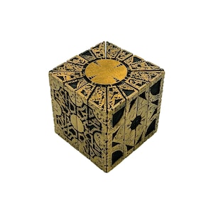 May include: A gold-colored metal puzzle box with intricate designs and a circular opening on the top. The box is closed and appears to be made of multiple interlocking pieces.
