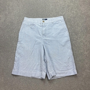 May include: Pale blue shorts with a button fastening and a small pocket. The shorts have a classic design and are made of a soft, textured fabric. The shorts have a small label with text.