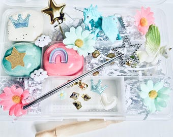 May include: A clear plastic storage box filled with various items for a sensory play activity. The box contains two containers of slime, a unicorn, a star, a crown, a wand, and several small decorative items. The box is perfect for imaginative play and sensory exploration.
