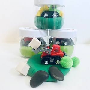 Pode incluir: Três frascos de vidro cheios de massa de modelar verde e veículos de construção de brinquedo. O frasco superior tem um caminhão basculante de brinquedo amarelo e verde. O frasco do meio tem um veículo de construção de brinquedo vermelho com um bloco branco. O frasco inferior tem um veículo de construção de brinquedo preto.