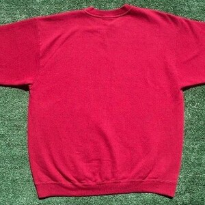 Może przedstawiać: Gładka czerwona bluza z okrągłym dekoltem i długimi rękawami. Odzież wykonana jest z miękkiego materiału i prezentowana na zielonej powierzchni. Bluza to klasyczny styl, odpowiedni do noszenia na co dzień.