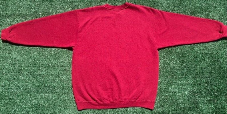 Może przedstawiać: Gładka czerwona bluza z okrągłym dekoltem i długimi rękawami. Odzież wykonana jest z miękkiego materiału i prezentowana na zielonej powierzchni. Bluza to klasyczny styl, odpowiedni do noszenia na co dzień.