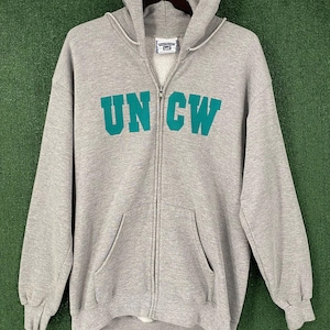 May include: A grey zip-up hoodie featuring the teal letters "UNCW". The hoodie has a hood, a full-length zip, and a kangaroo pocket. The brand label "Lee" is visible at the top.