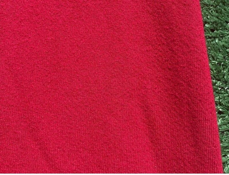 Może przedstawiać: Zbliżenie na żywy czerwony materiał z teksturowanym wzorem dzianiny. Materiał jest w jednolitym kolorze, bez widocznych wzor&oacute;w i deseni. Tkanina jest prawdopodobnie tekstylna, być może do odzieży lub wystroju domu.