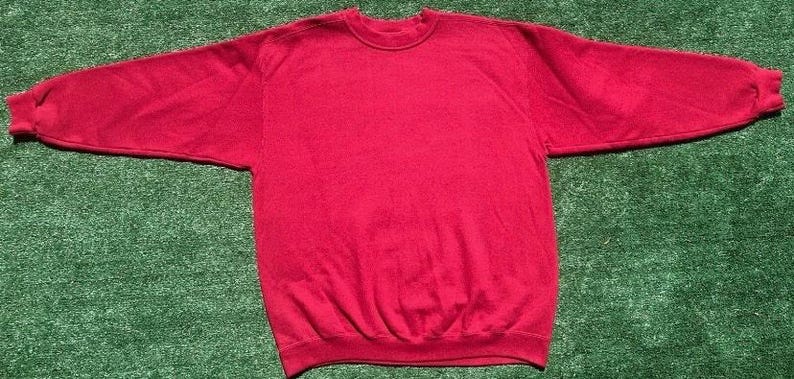 Może przedstawiać: Gładka czerwona bluza z okrągłym dekoltem i długimi rękawami. Odzież wykonana jest z miękkiego materiału i leży płasko na zielonej powierzchni. Rękawy są rozłożone na boki.