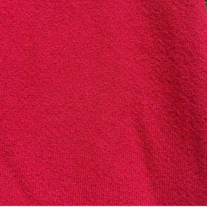 Może przedstawiać: Zbliżenie fragmentu czerwonej tkaniny. Materiał ma teksturowany wygląd z widocznym wzorem dzianiny. Kolor jest żywy, jednolity czerwony, wypełniający kadr. Tkanina wydaje się miękka i prawdopodobnie dzianinowa.
