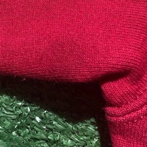 Może przedstawiać: Zbliżenie fragmentu czerwonej dzianiny, ukazujące fakturę i szczeg&oacute;ły szw&oacute;w. Tkanina wydaje się miękka, prawdopodobnie mieszanka bawełny lub wełny, o lekko nier&oacute;wnej powierzchni. Obraz podkreśla konstrukcję materiału.