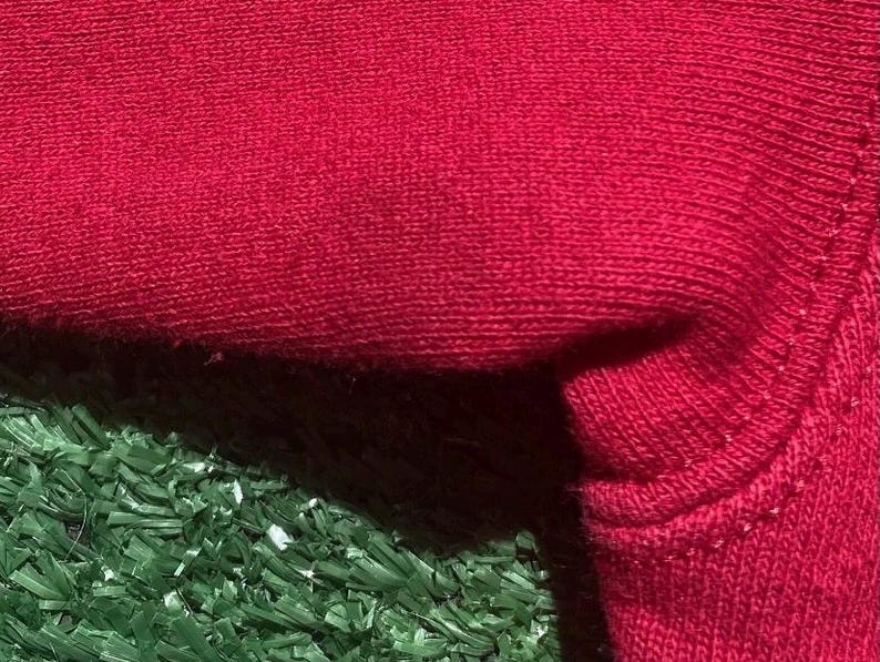 Może przedstawiać: Zbliżenie fragmentu czerwonej dzianiny, ukazujące fakturę i szczeg&oacute;ły szw&oacute;w. Tkanina wydaje się miękka, prawdopodobnie mieszanka bawełny lub wełny, o lekko nier&oacute;wnej powierzchni. Obraz podkreśla konstrukcję materiału.