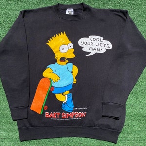 Puede incluir: Sudadera negra con Bart Simpson y un monopatín. Bart tiene piel amarilla, pantalones cortos azules y una camisa azul claro. El bocadillo de diálogo dice: "COOL YOUR JETS, MAN!"