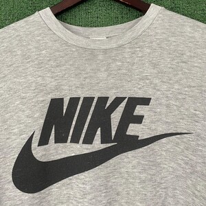 May include: A heather gray crew neck sweatshirt with the black Nike logo and swoosh. The sweatshirt is hanging on a wooden hanger against a green background.