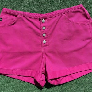 May include: Pink denim shorts with a button fly and cuffed hems.