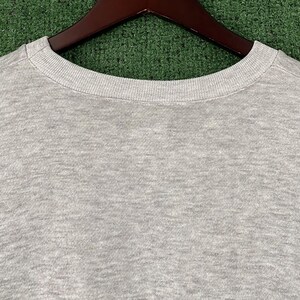 May include: A heather gray crew neck sweatshirt, displayed on a wooden hanger against a green background. The close-up shot highlights the texture of the fabric and the ribbed neckline. The sweatshirt is a casual apparel item.