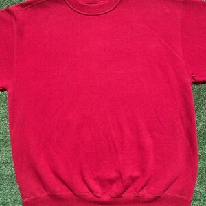 Może przedstawiać: Gładka, czerwona bluza z okrągłym dekoltem. Bluza ma prążkowany kołnierz, mankiety i d&oacute;ł. Widoczne są kr&oacute;tkie rękawy. Odzież wykonana jest z miękkiego, wygodnego materiału.