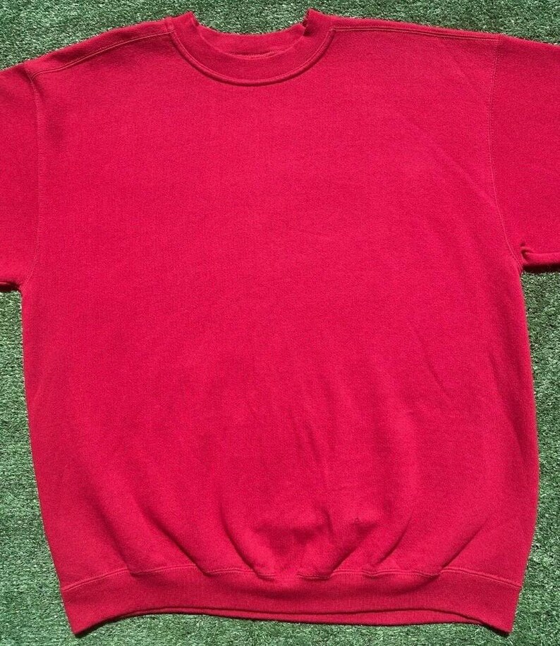 Może przedstawiać: Gładka, czerwona bluza z okrągłym dekoltem. Bluza ma prążkowany kołnierz, mankiety i d&oacute;ł. Widoczne są kr&oacute;tkie rękawy. Odzież wykonana jest z miękkiego, wygodnego materiału.