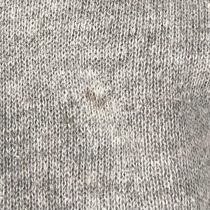 May include: Close-up of a grey knitted fabric with a textured surface. The fabric appears to be a blend of light and dark grey yarns, creating a heathered effect. The knit pattern is visible, showing the individual stitches.