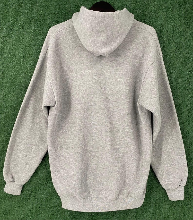 May include: A grey hoodie with a hood and long sleeves. The sweatshirt is hanging on a black hanger against a green background. The cuffs and bottom hem are ribbed.