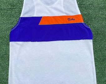 May include: White athletic vest with a blue and orange horizontal stripe across the chest. The word "Tinley" is printed in blue on the orange stripe. The vest is sleeveless and has a scoop neck.