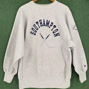 Puede incluir: Sudadera Champion gris claro con la palabra "SOUTHAMPTON" en azul marino arqueada sobre el pecho. Debajo, dos remos cruzados. La manga tiene la palabra "SOUTH" y un logotipo.