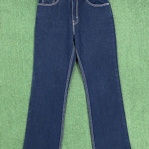 May include: Dark blue denim jeans with a flared leg. The jeans feature a classic five-pocket design, white stitching, and a button and zip closure. The label reads "FLARE".