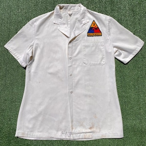 May include: Off-white short-sleeved shirt with a button-down front and a chest pocket. A colorful patch with the text "HELL ON WHEELS" and the number "2" is on the upper left chest. The shirt shows signs of wear.